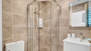 Een moderne badkamer met een douchecabine van glas, een wit wastafelmeubel met spiegel en beigetinten tegels.