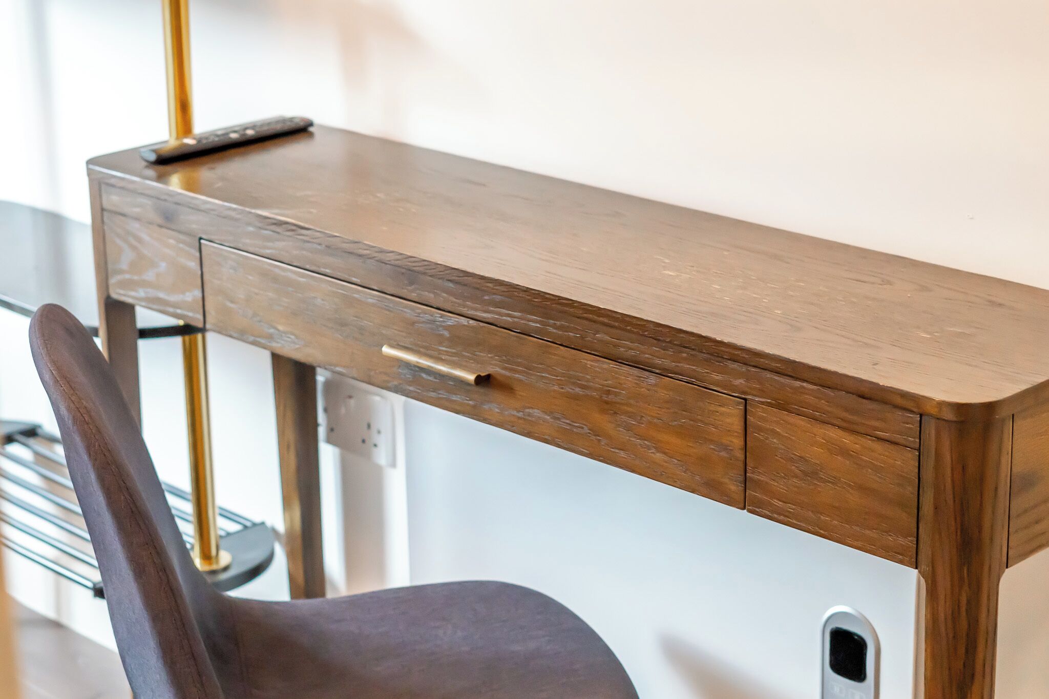 A wooden desk with a drawer and a remote control on top.