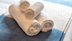Drie opgerolde handdoeken op een bed met een blauw-witte gestreepte deken.