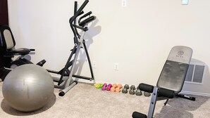 Ein Heim-Fitnessraum mit einem Ergometer, einem Rudergerät, einem Medizinball und einer Hantelbank.