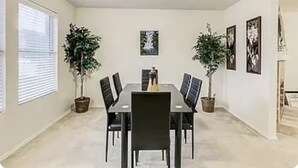 Ein Esszimmer mit einem rechteckigen Tisch, schwarzen Stühlen, Topfpflanzen und gerahmten Bildern an den Wänden.
