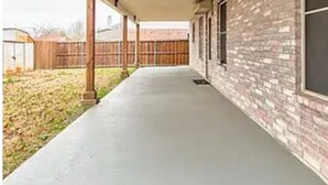 Ein überdachter Außenbereich mit Betonboden, Holzbalken und einer Ziegelwand.