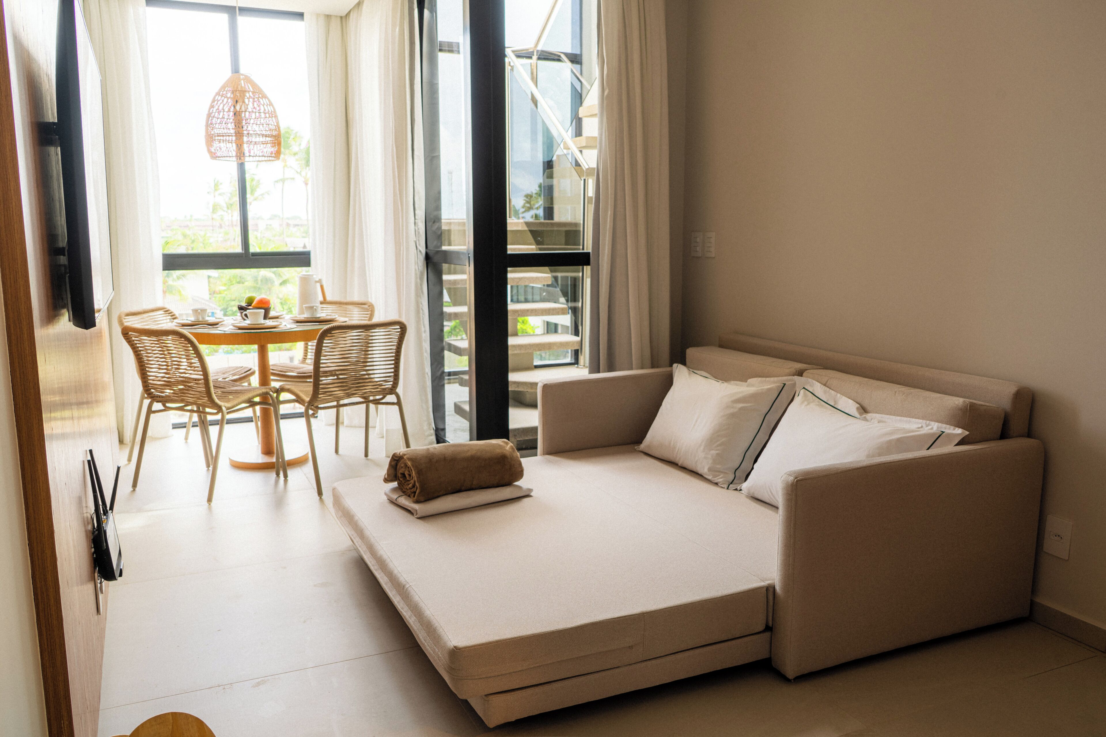 Una camera moderna con un divano letto, un tavolo da pranzo con sedie e vista su un edificio.