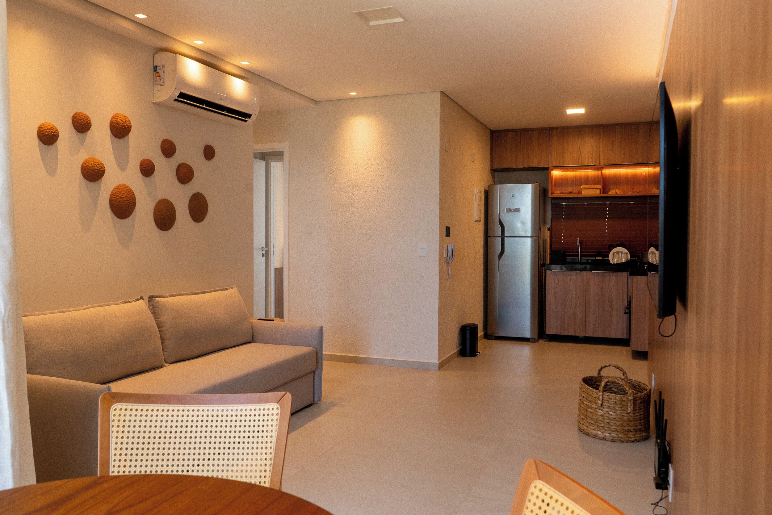 A modern living room with a sofa, a dining table, and a kitchen area with wooden cabinets and a refrigerator.