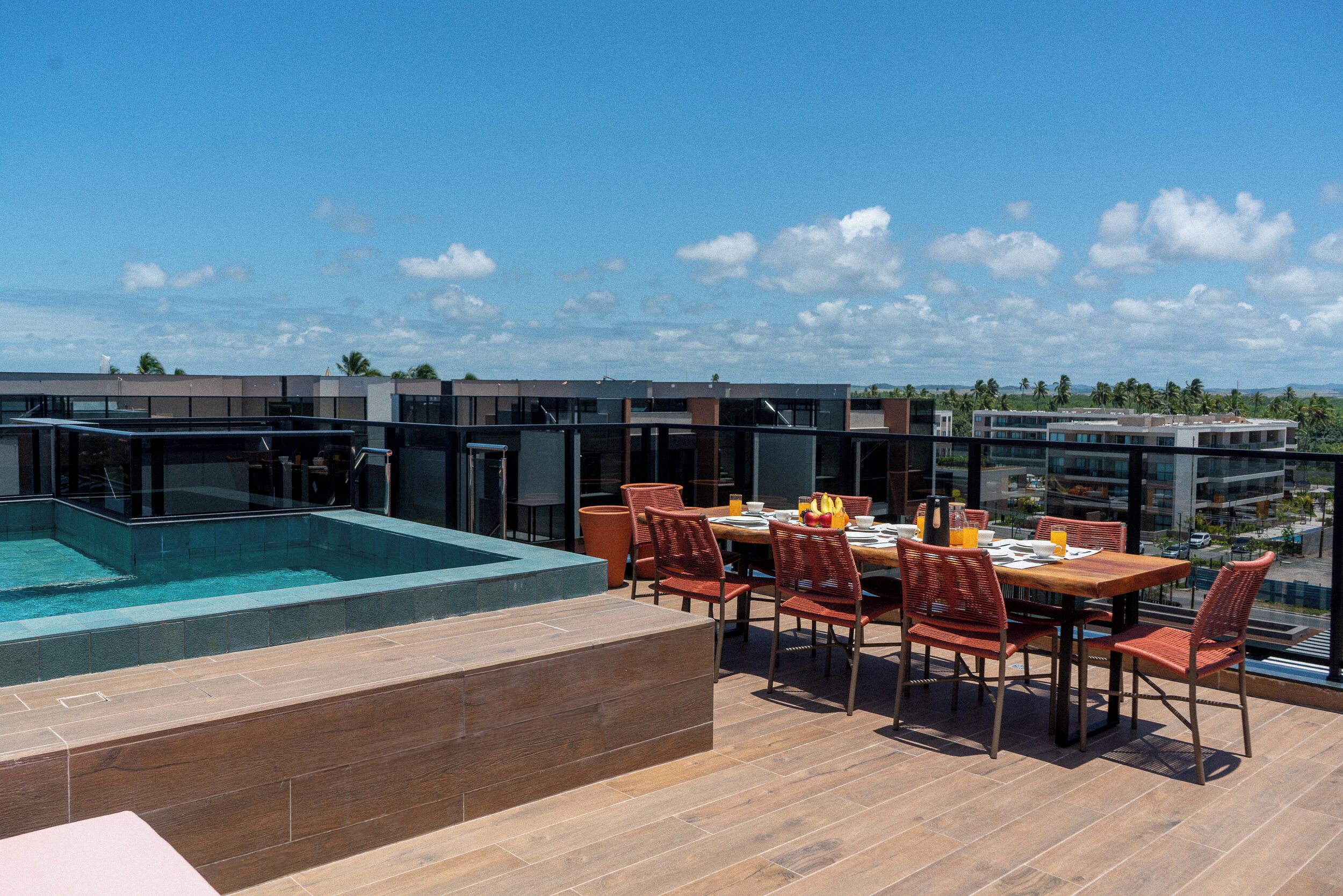 A rooftop terrace with a pool, dining area, and modern buildings in the background.