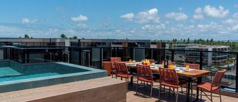 A rooftop terrace with a pool, dining area, and modern buildings in the background.