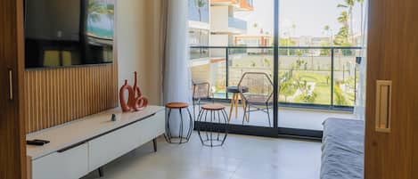 Una habitación de hotel moderna con una tele grande, un balcón con sillas y una cama.