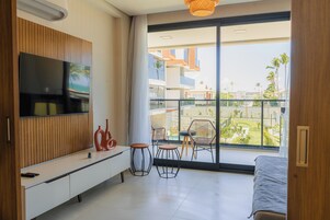 Una habitación de hotel moderna con una tele grande, un balcón con sillas y una cama.