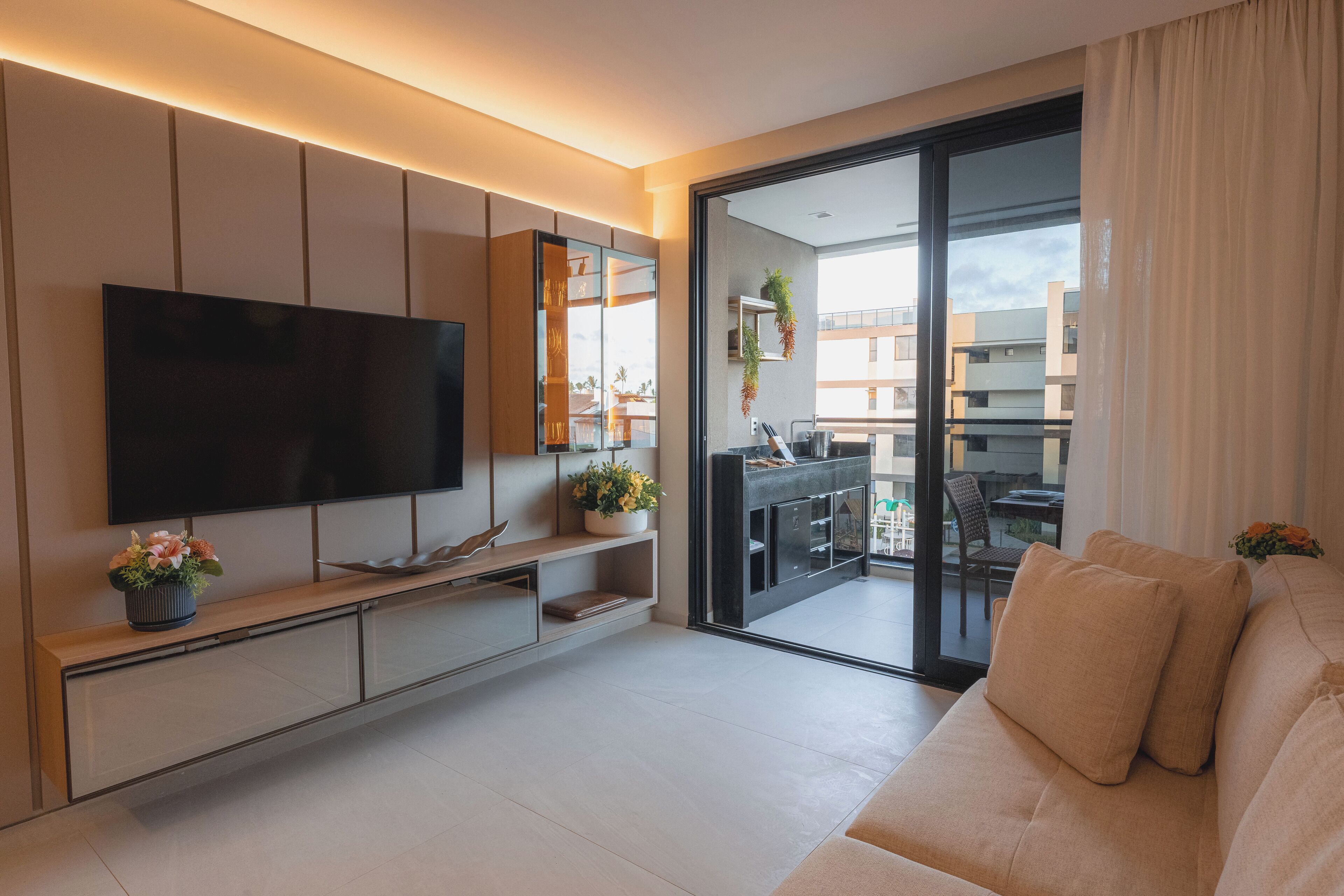 A modern living room with a flat-screen TV, a sofa, a coffee table, and a balcony with a view of the city.
