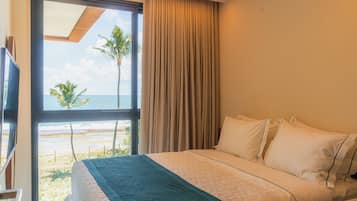 A hotel room with a bed, a large window with a view of the beach and palm trees, and a curtain.