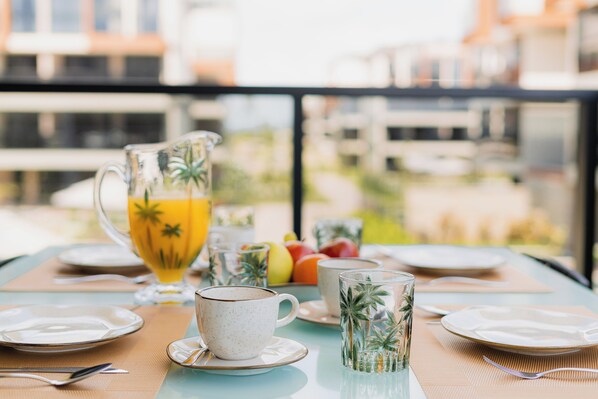 A breakfast table set with plates, cups, and a pitcher of orange juice. - Cais Eco ResidĂȘncia Muro Alto by Sintta (Ipojuca)