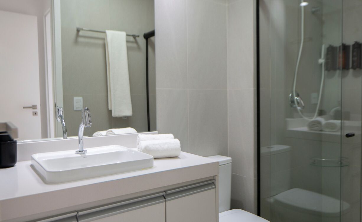 A modern bathroom with a white sink, two faucets, a glass shower enclosure, and a towel rack with a white towel.