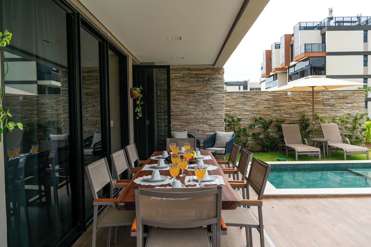 Un comedor con ambiente junto a la piscina, con una mesa dispuesta para seis personas, vasos de jugo de naranja y sillas alrededor.
