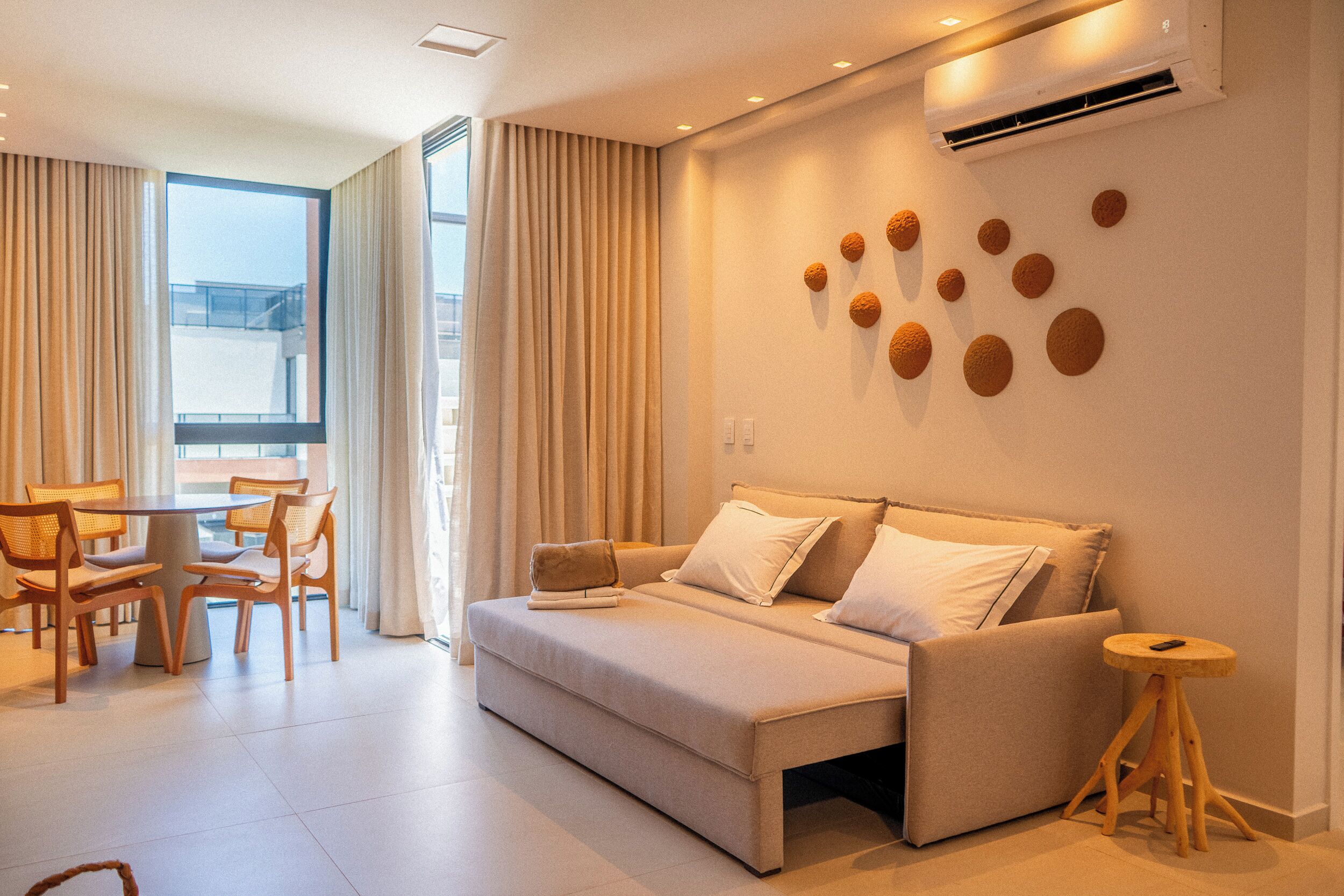 Una moderna camera d'albergo con una divano letto, un'area pranzo con tavolo e sedie, e un'ampia finestra con tende.