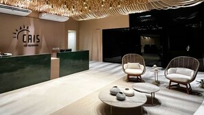 A modern reception area with a reception desk, two wicker chairs, a round table, and a decorative ceiling light fixture. - Cais Eco Residência Muro Alto by Sintta (Ipojuca)