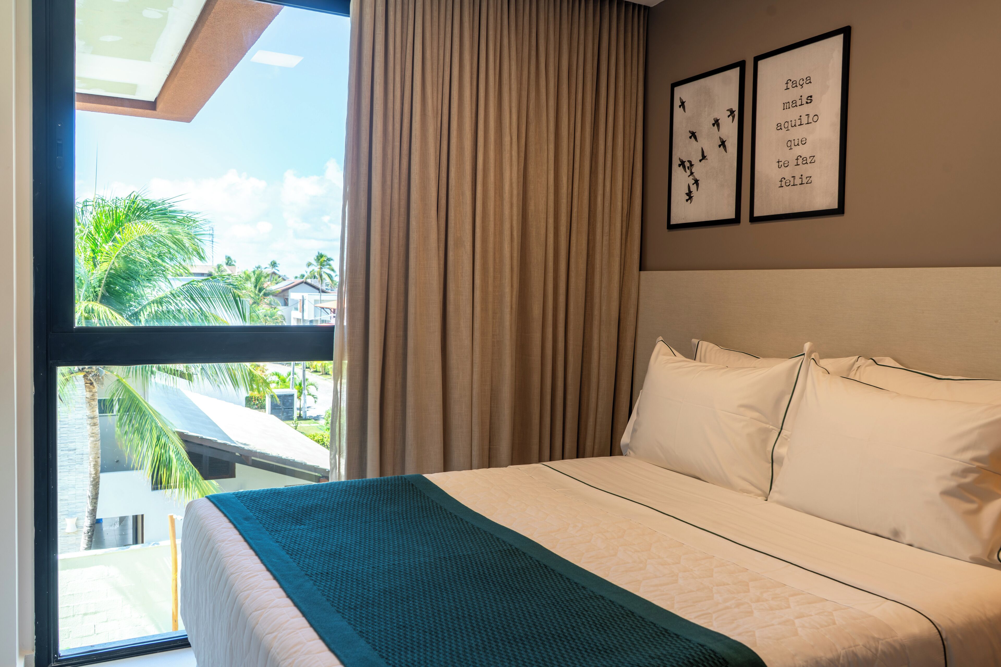 Ein Hotelzimmer mit einem großen Bett, Blick auf Palmen und Gebäude, sowie zwei gerahmte Bilder an der Wand.