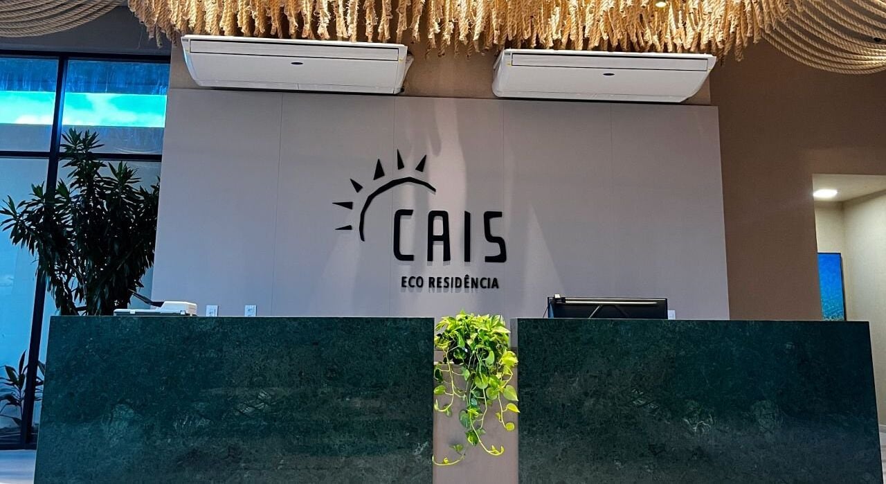 Un comptoir d’accueil orné du logo de « CAIS ECO RESIDENCIA » et agrémenté d’une plante suspendue.
