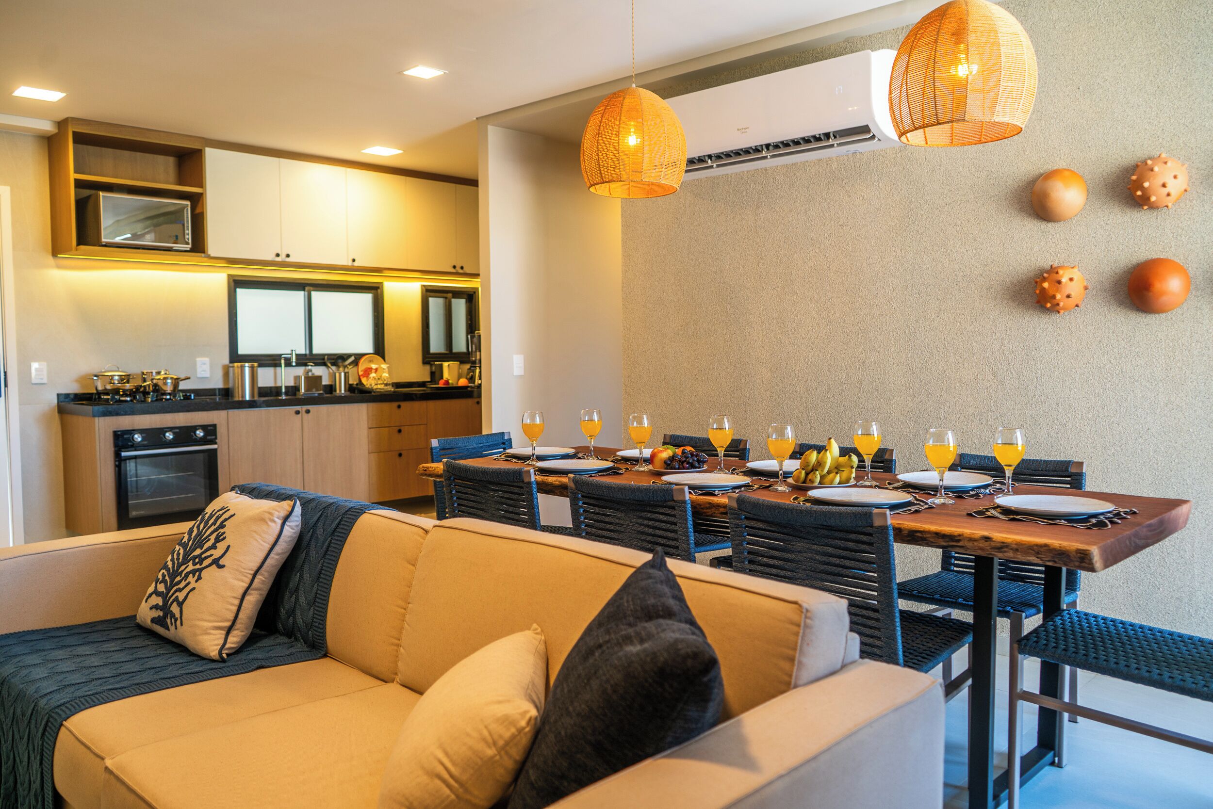 A modern kitchen with built-in appliances, a dining area with a wooden table and chairs, and a sofa with cushions.