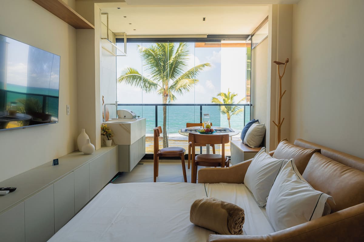 Una habitación de hotel con balcón, cama, zona de estar y televisor en la pared.
