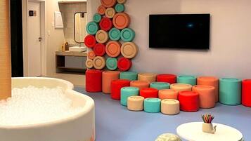 Un baño moderno con una bañera grande llena de burbujas, un televisor montado en la pared y una colorida disposición de jabones.