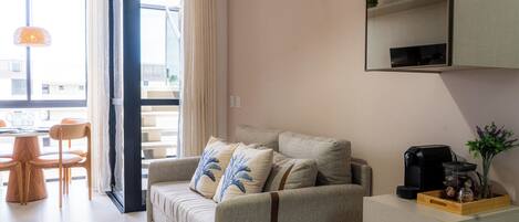 A modern living room with a sofa, a coffee machine, and a dining area with chairs and a table.