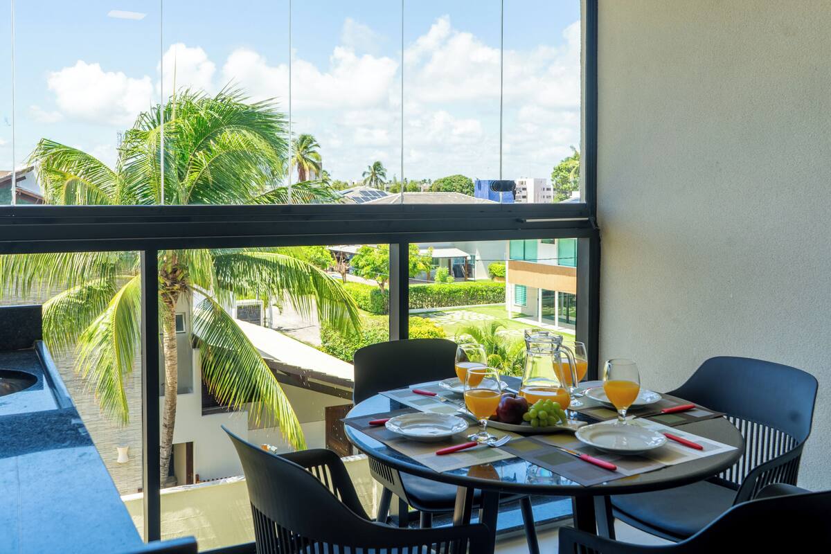 Comedor con una mesa lista para dos personas, con vistas a un jardín exuberante y palmeras.