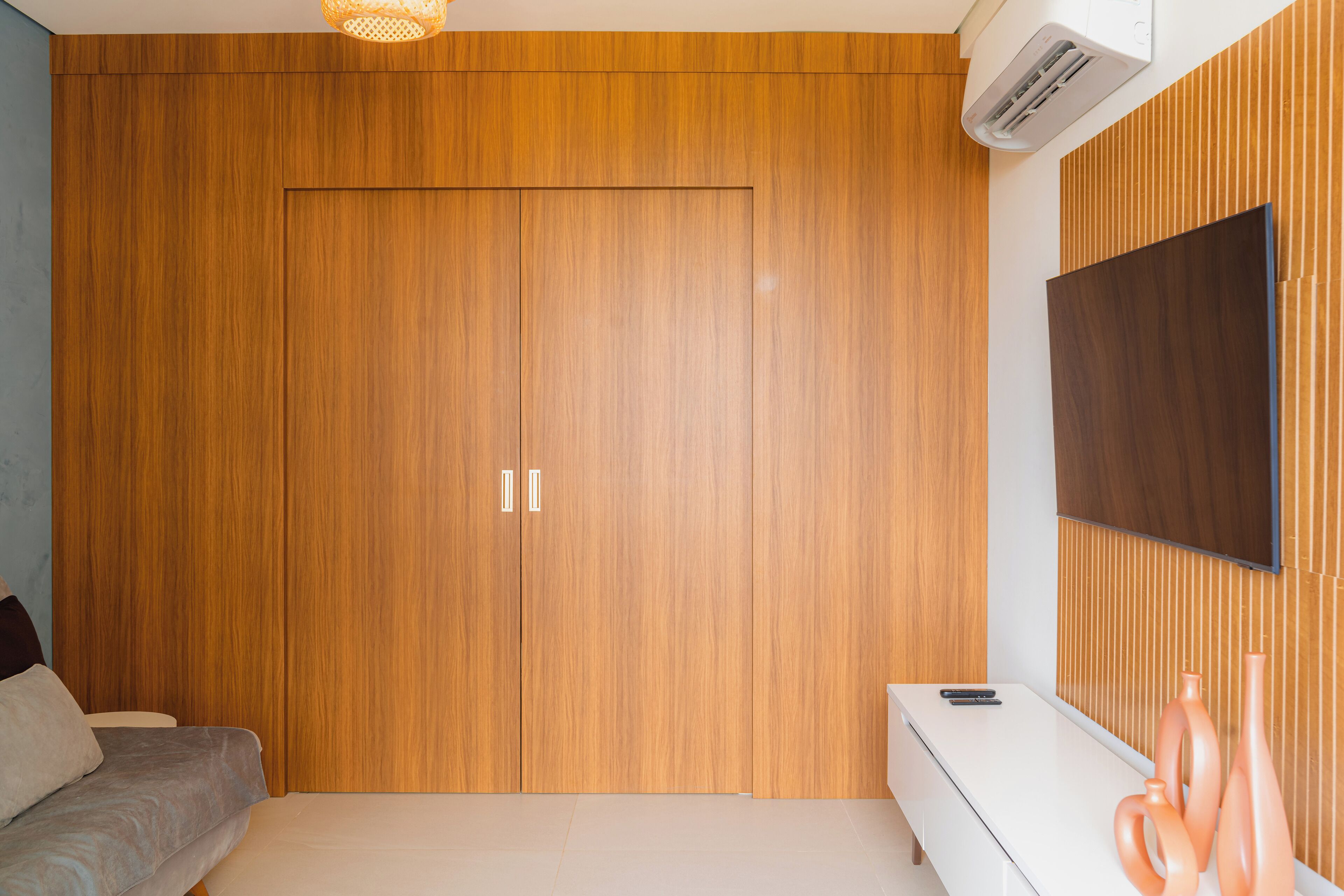A bedroom with a wooden wardrobe, a flat-screen TV, a sofa, and a bedside table.