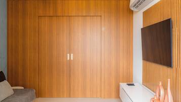 Un dormitorio con un armario de madera, un televisor de pantalla plana, un sofá y una mesita de noche.