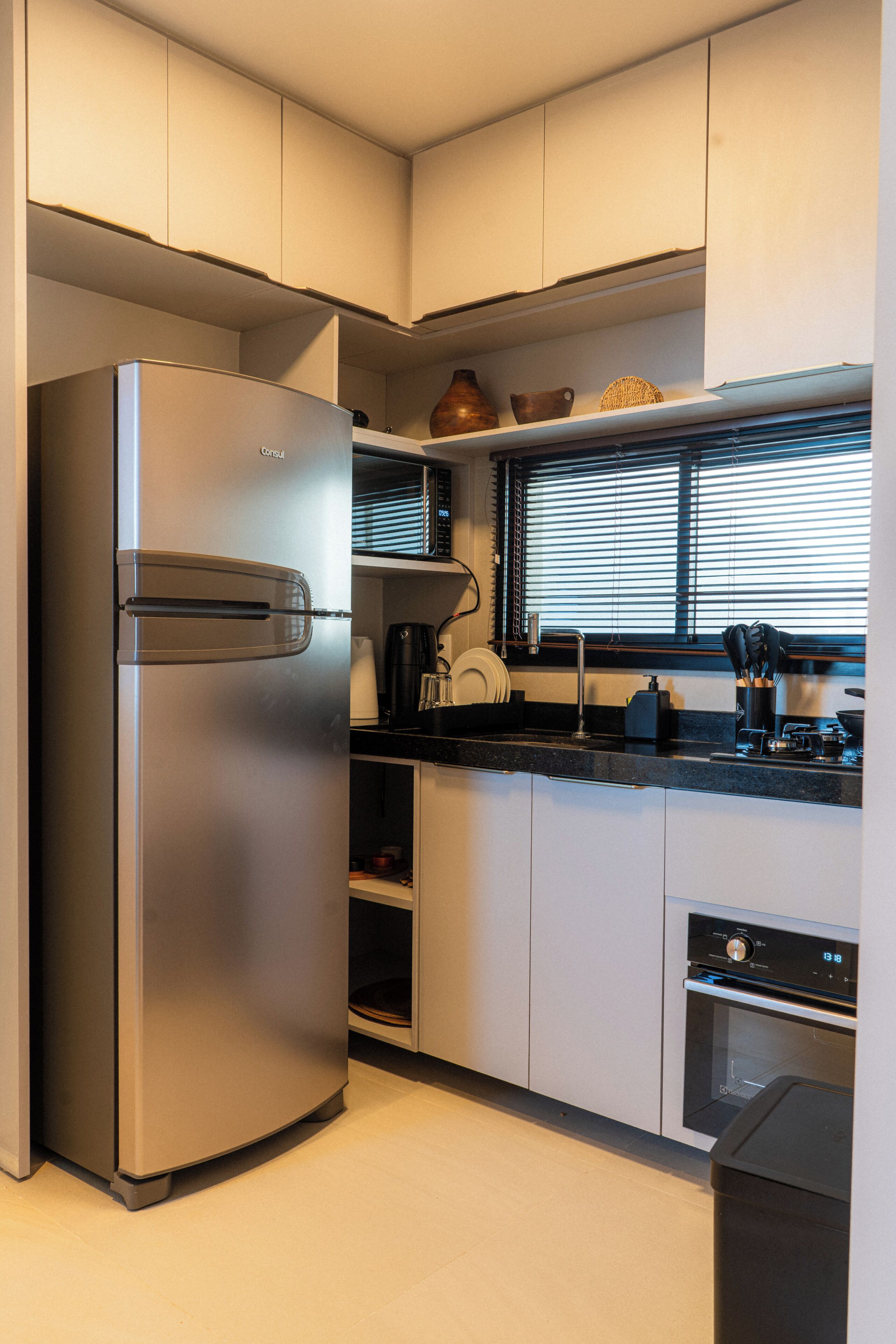 Una cocina moderna con electrodomésticos de acero inoxidable, horno empotrado y ventana con persianas.