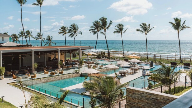 A resort with a pool area, lounge chairs, and palm trees. - Cais Eco Residência Muro Alto by Sintta (Ipojuca)