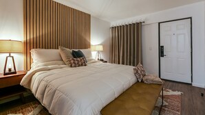 A bedroom with a large bed, two bedside tables with lamps, a door, and a curtain. - Modern King Room with Plush Bedding – Perfect for Business or Leisure Stays! (San Angelo)