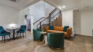 Una sala de estar moderna con una escalera, un sofá de cuero, sillones color aguamarina y una mesita con una lámpara.