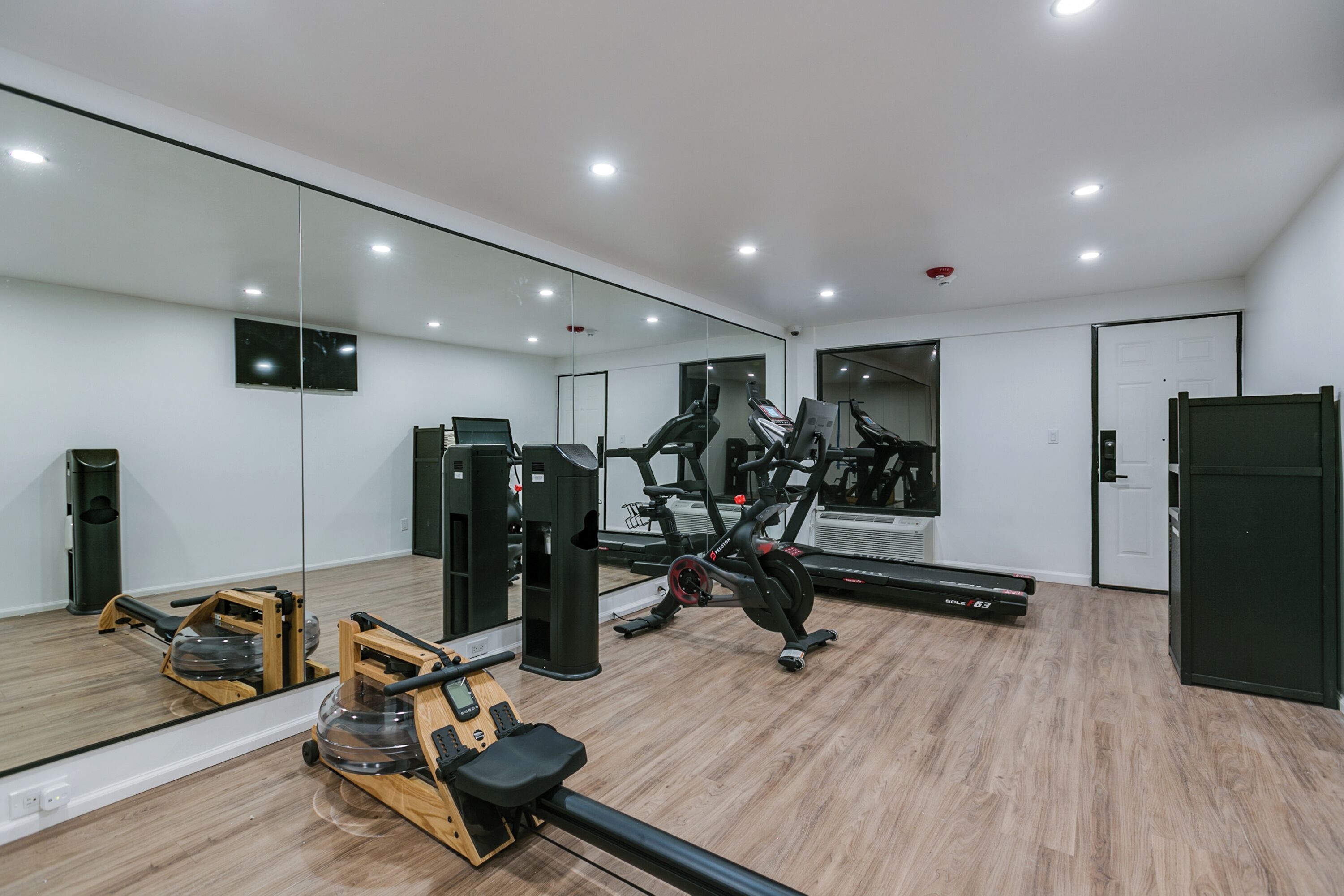 Et moderne fitnesscenter med træningsudstyr, et stort spejl og trægulv.