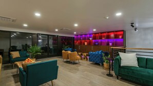 Una sala moderna con sofás verde azulado y verde, una mesa de centro con naranjas y un mueble iluminado con luz roja.