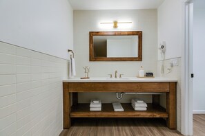 Un bagno con un mobile bagno in legno, piastrelle bianche, uno specchio, un portasciugamani e un asciugacapelli.