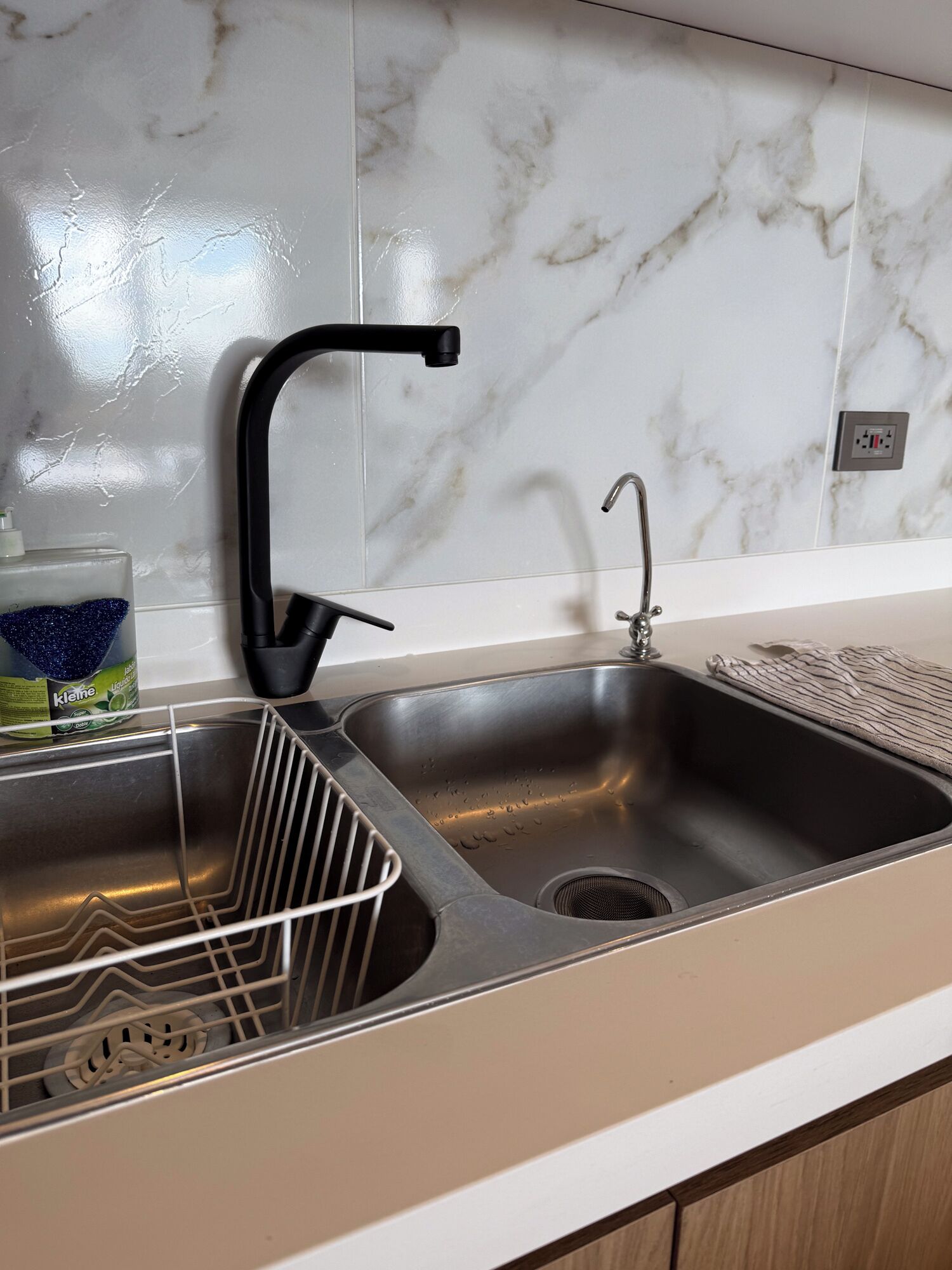 A kitchen with a double stainless steel sink, a black faucet, and a bottle of Kleen dish soap on the counter.