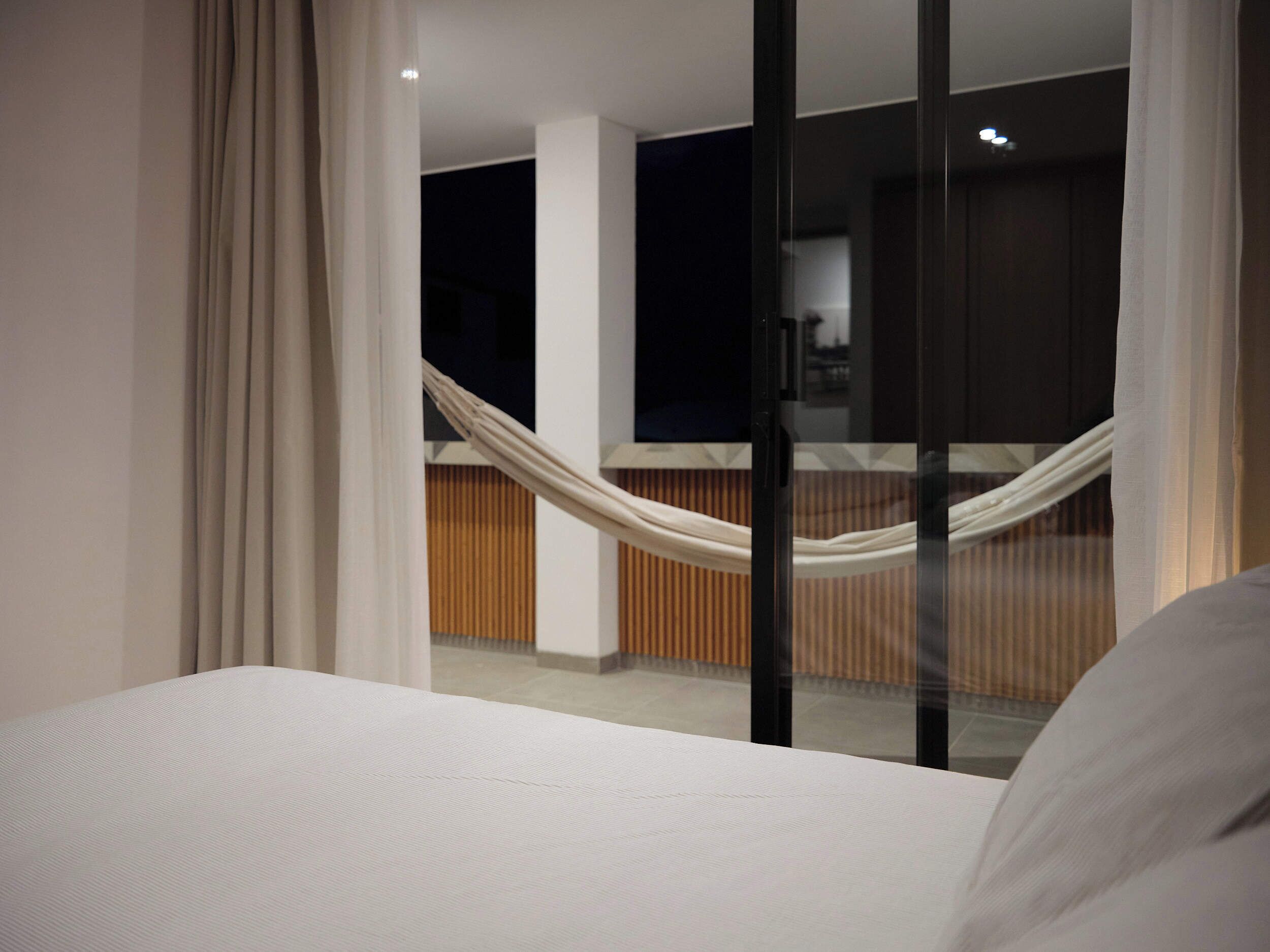Een moderne hotelkamer met een groot bed, uitzicht op het interieur door een glazen deur en een hangmat op de achtergrond.