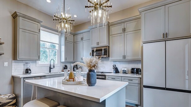 Una cocina moderna con armarios blancos, una isla central con taburetes, electrodomésticos de acero inoxidable y un florero decorativo.