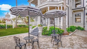 Un patio con mobiliario exterior y sombrillas, un edificio blanco con balcones y una estructura en forma de cúpula al fondo.