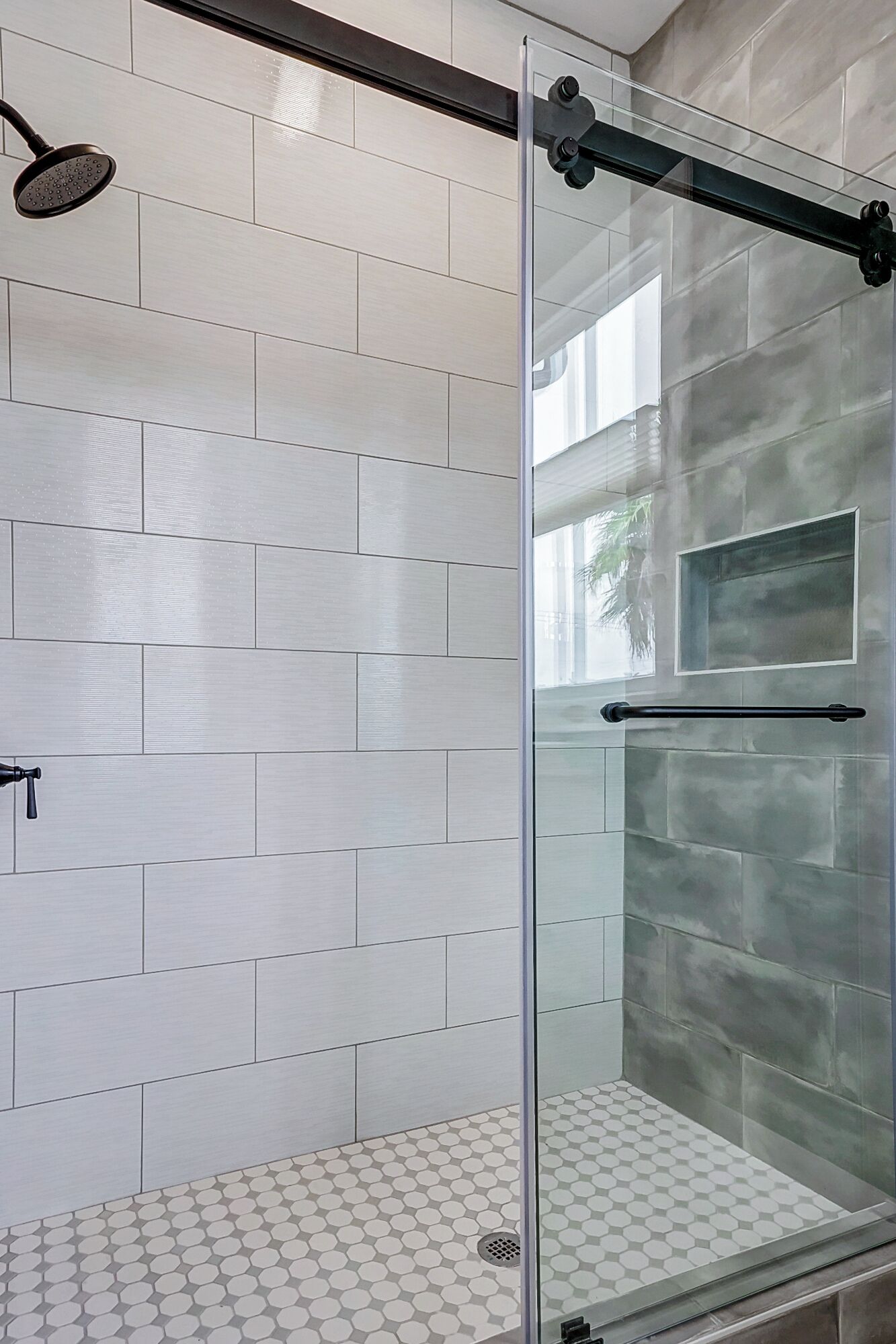 A glass-enclosed shower with a rain showerhead, white tiled walls, and a hexagonal patterned floor.