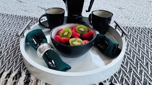 Bandeja de desayuno con fruta y café en una cama con vistas a la vegetación.