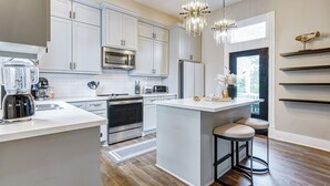 Una cocina moderna con armarios blancos, electrodomésticos de acero inoxidable y una isla central con taburetes.