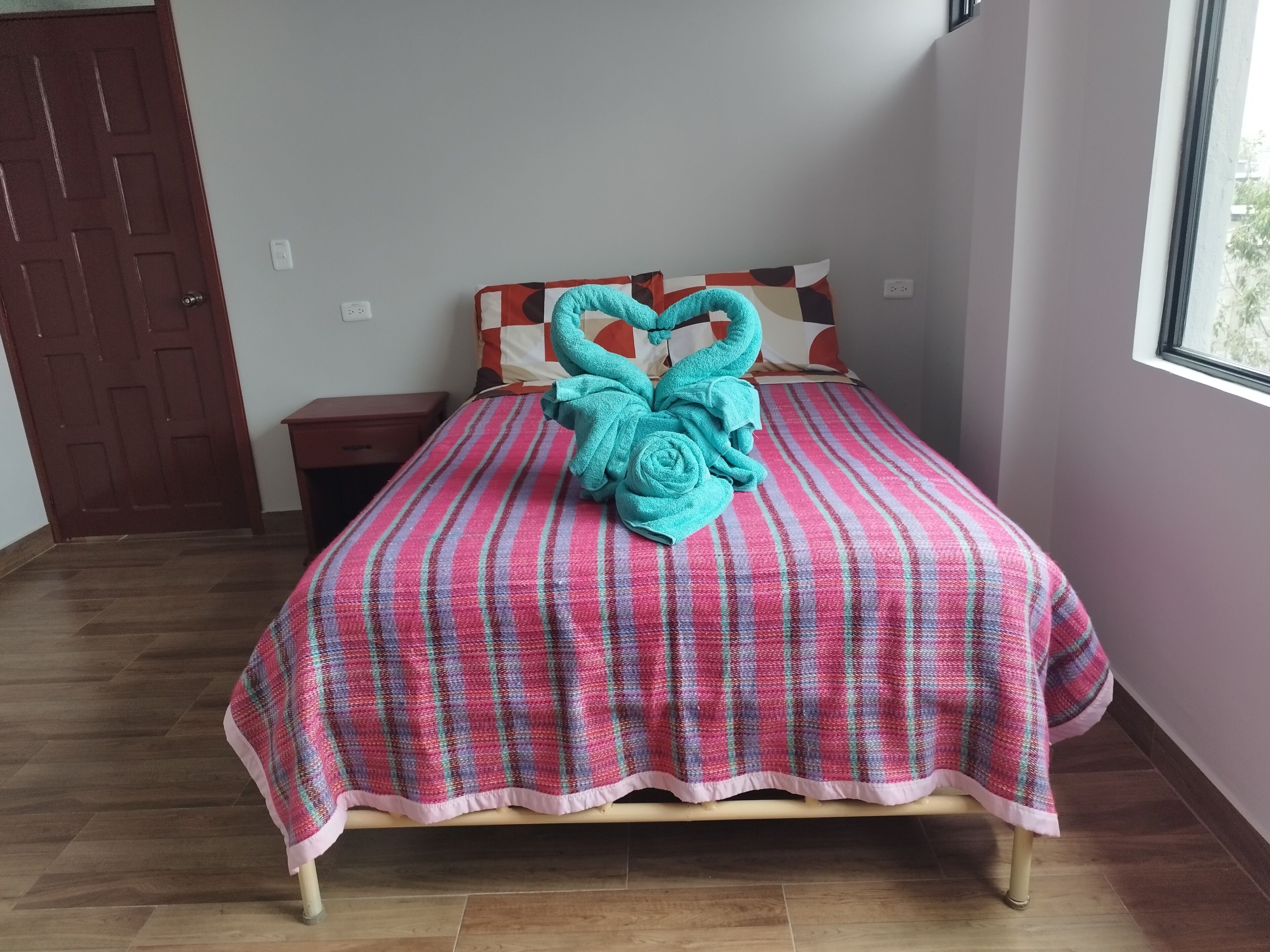 Un letto rifatto con una coperta a righe e un asciugamano color petrolio disposto a forma di cuore.