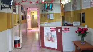 A reception area with a glass partition, a poster of a woman, and a vase of red roses on a wooden table. - Hostal Terranova Quitumbe (Quito)