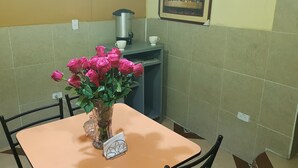 A dining area with a table, chairs, a vase of pink roses, a coffee machine, and a framed picture on the wall. - Hostal Terranova Quitumbe (Quito)