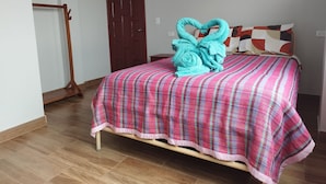 A bedroom with a bed, a wooden floor, a door, and a wall with a light switch. - Hostal Terranova Quitumbe (Quito)