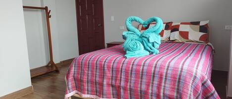 Un dormitorio con cama, piso de madera, una puerta y una pared con interruptor de luz.