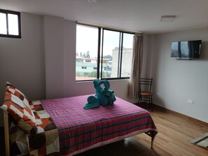 Um quarto com cama, uma cadeira, televisão e janela com vista para edifícios.