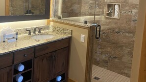 A modern bathroom with a granite countertop sink, a large mirror, and a walk-in shower with a glass door.