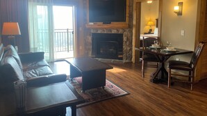 A living room with a stone fireplace, a flat-screen TV mounted above it, a sofa, a coffee table, and a dining area with a table and chairs.